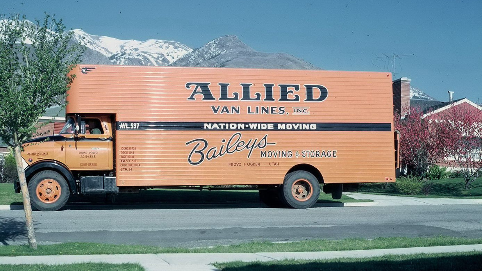 Historical colored image of a Bailey's Moving and Storage truck parked in front of mountains. 