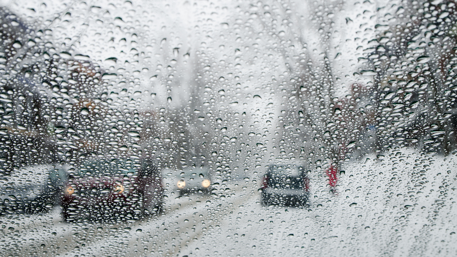 Blurry image through a frosted and rain-soaked window of a street with parked cars. The setting is snowy and bleak.