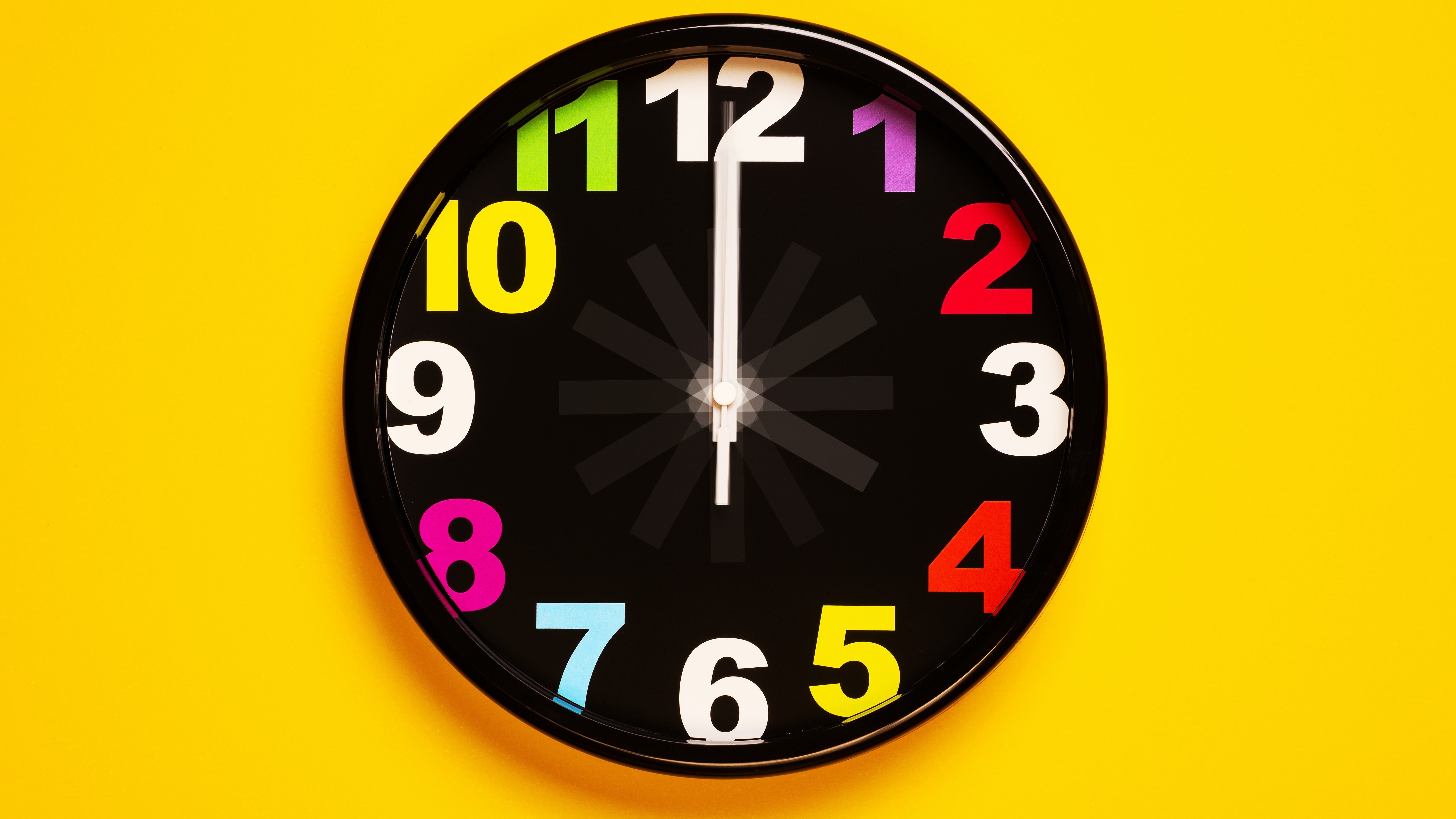 A large analog clock sits on a yellow wall. The hands are blurry, as if they're spinning very fast.