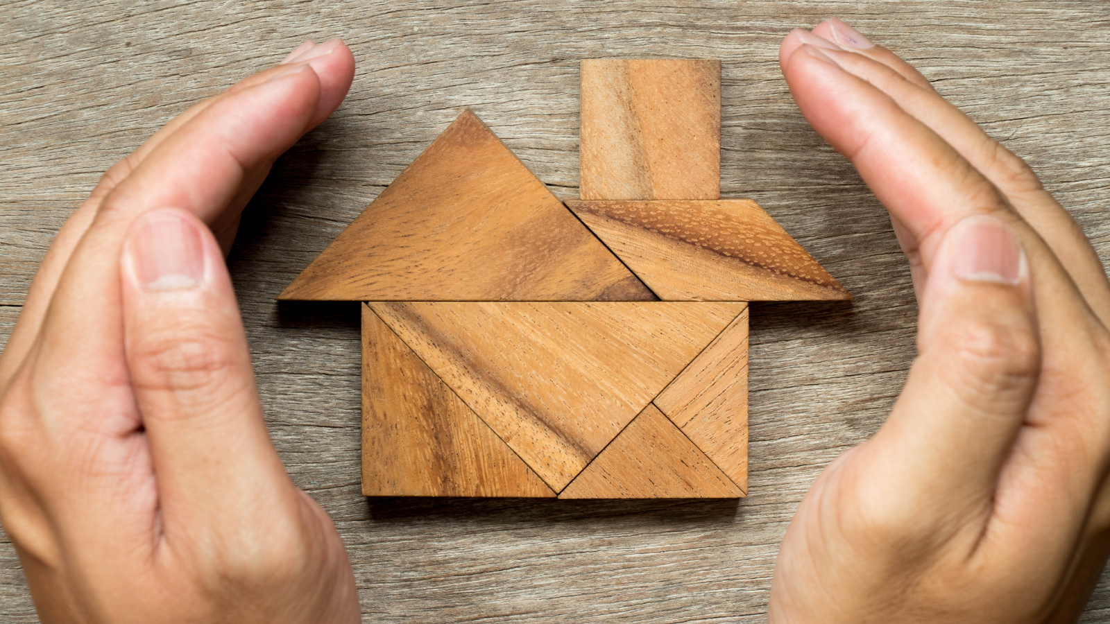 Image of two hands framing wooden blocks shaped to look like a house
