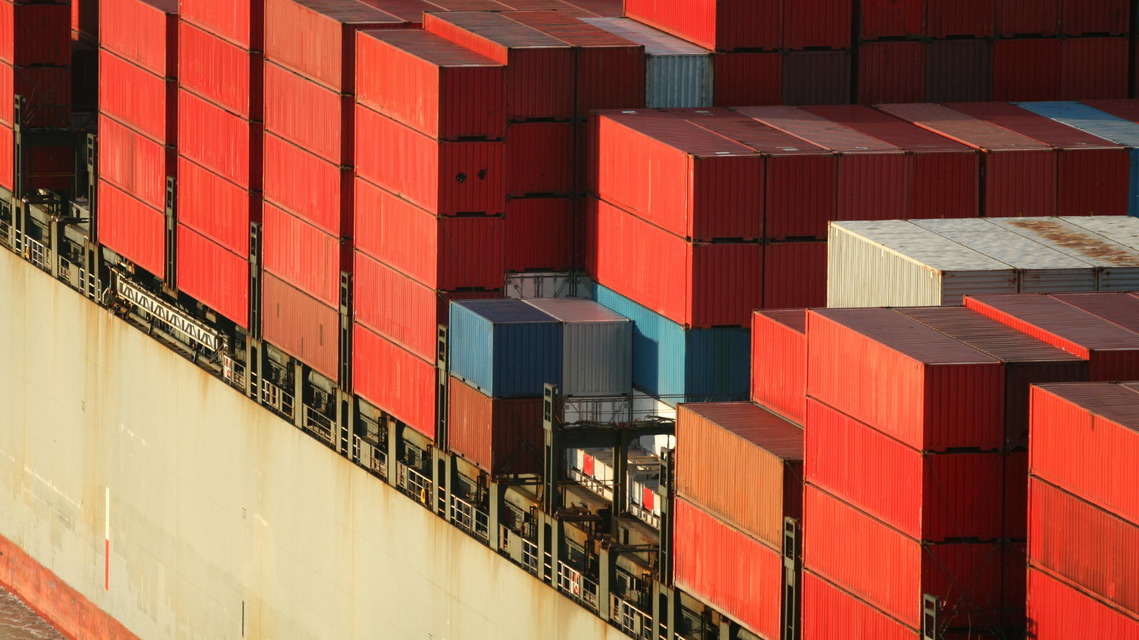 Image of numerous loaded red and blue shipping containers on a sea freight.